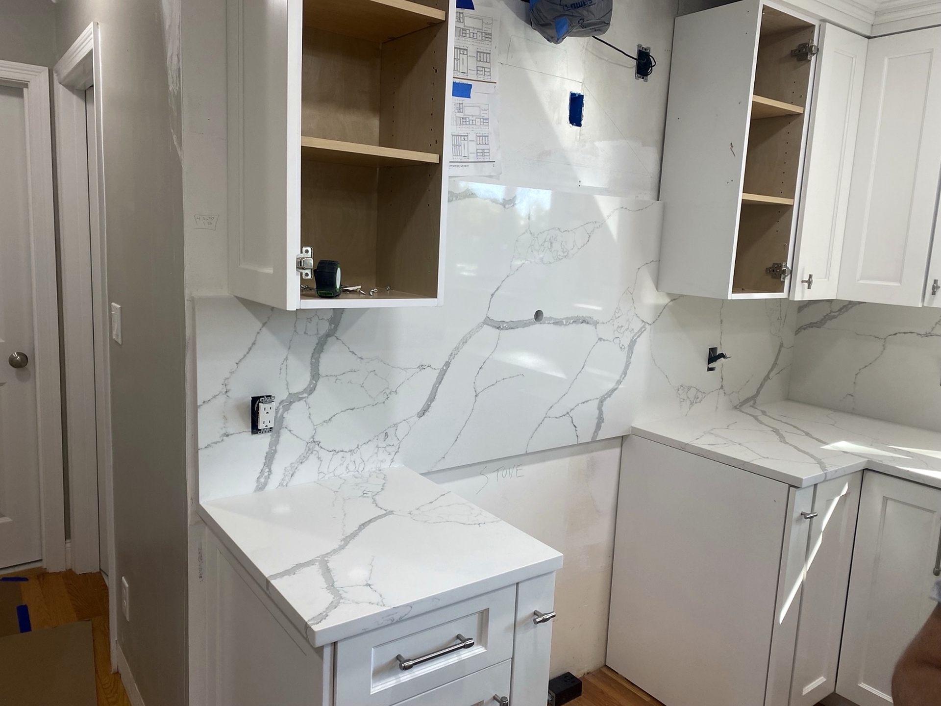 White kitchen with veined stone countertops and a matching full-height backsplash under the cabinets