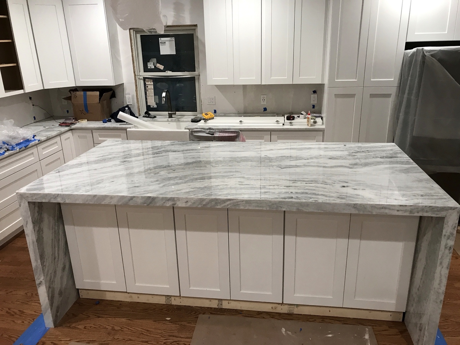 Large grey and white natural stone waterfall island being installed in a white kitchen
