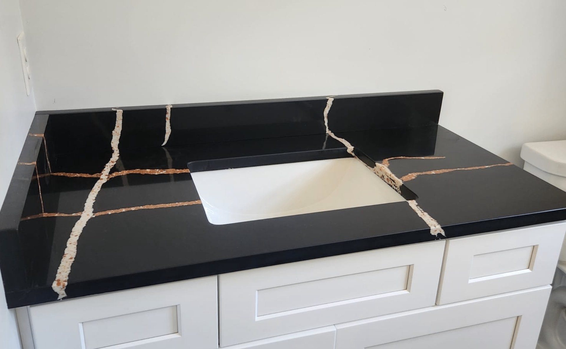 White vanity with a black stone countertop, bold white and copper veining and matching backsplash